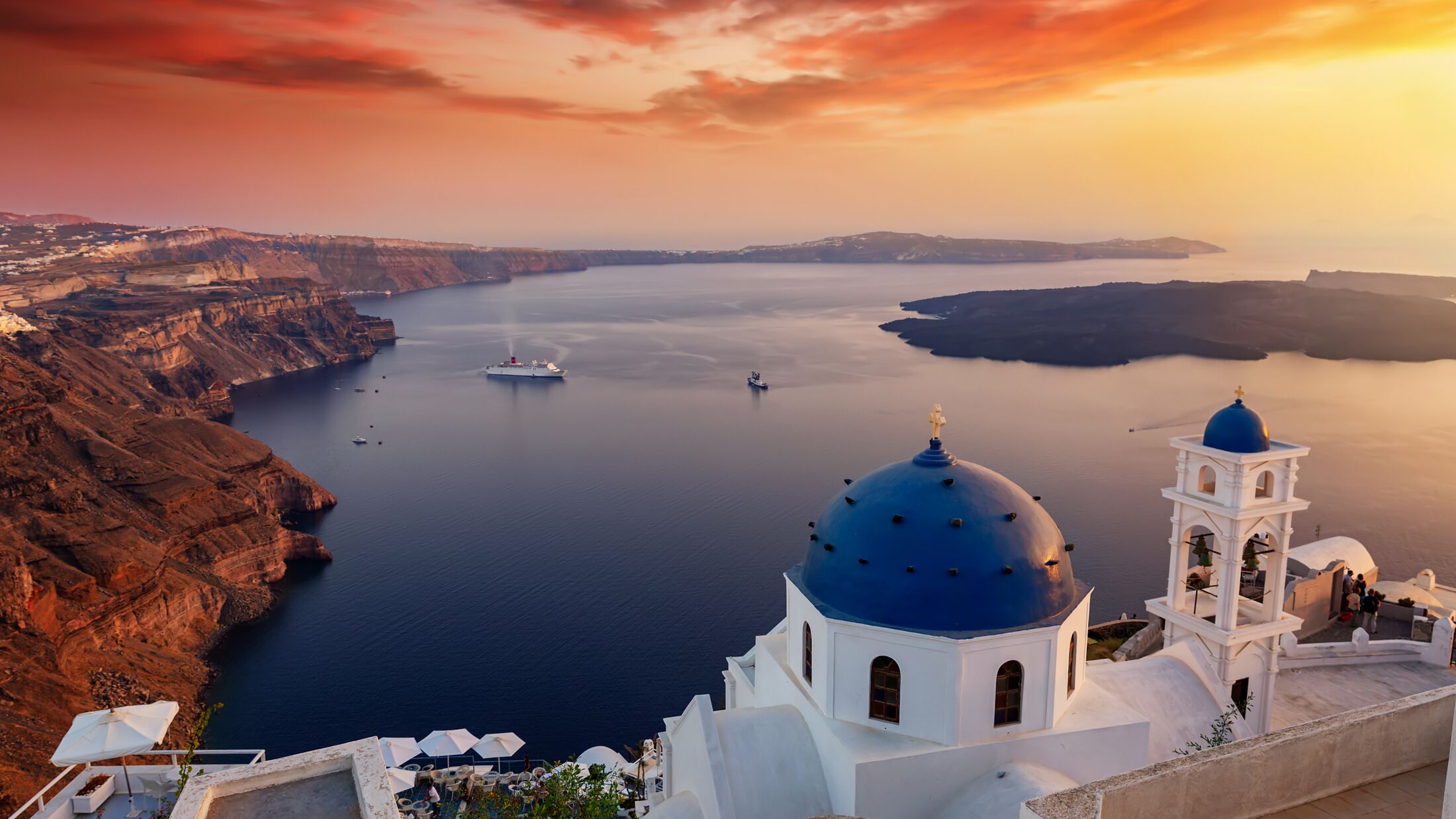 Sunset over the island of Santorini with blue domes of the churches and white houses at the village of Imerovigli, Cyclades, Greece