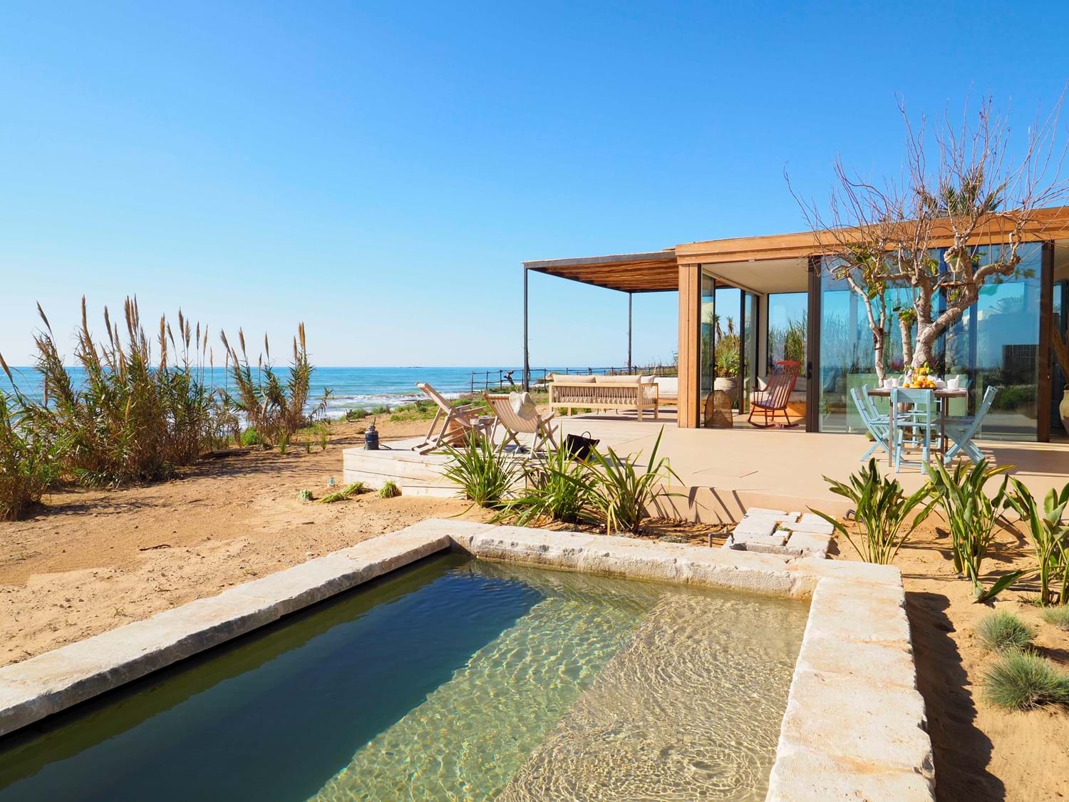 picture of a wooden beach house on sandy dunes with a small outdoor pool and blue sky