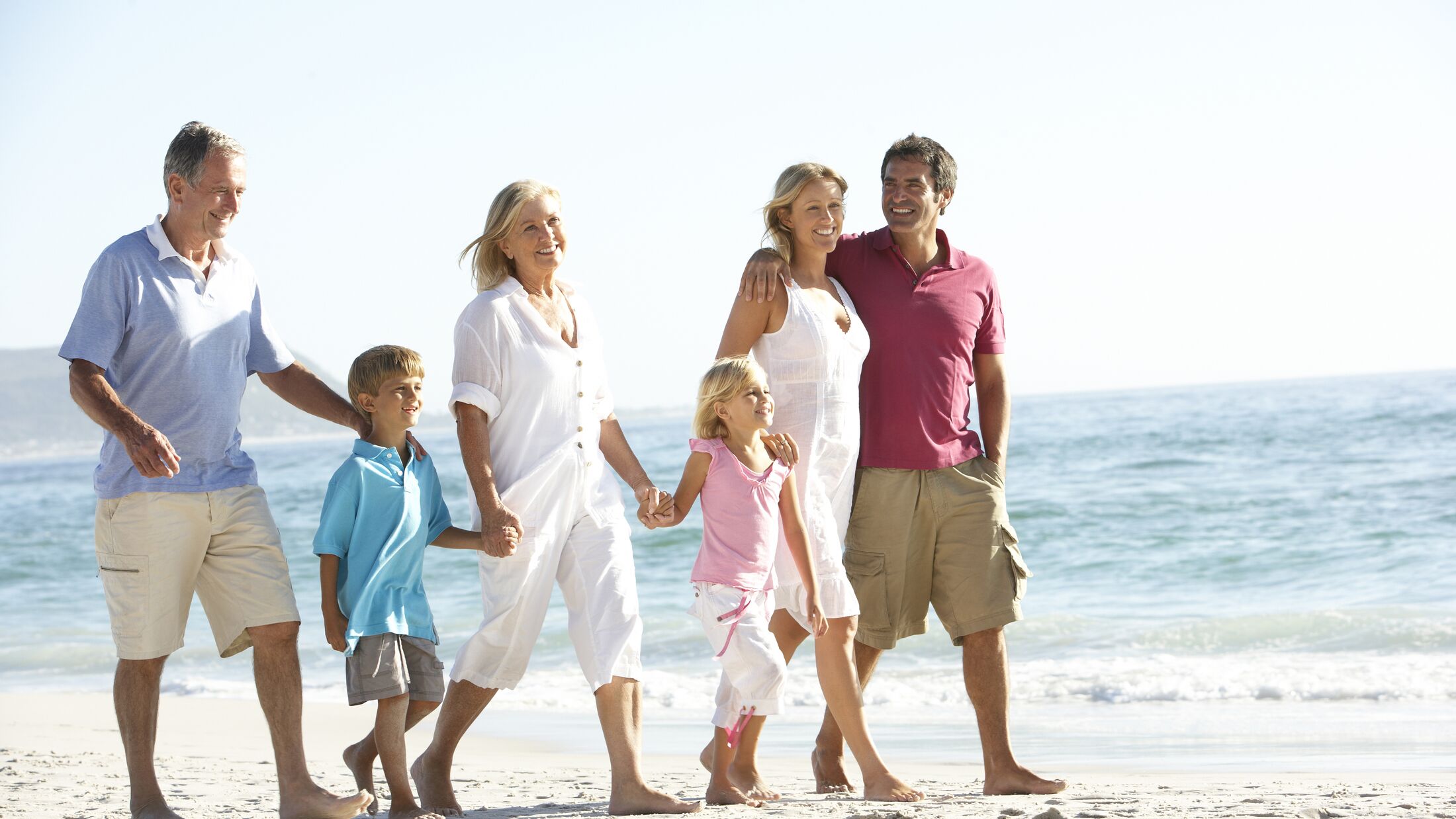 Three Generation Family On Holiday Walking On Beach