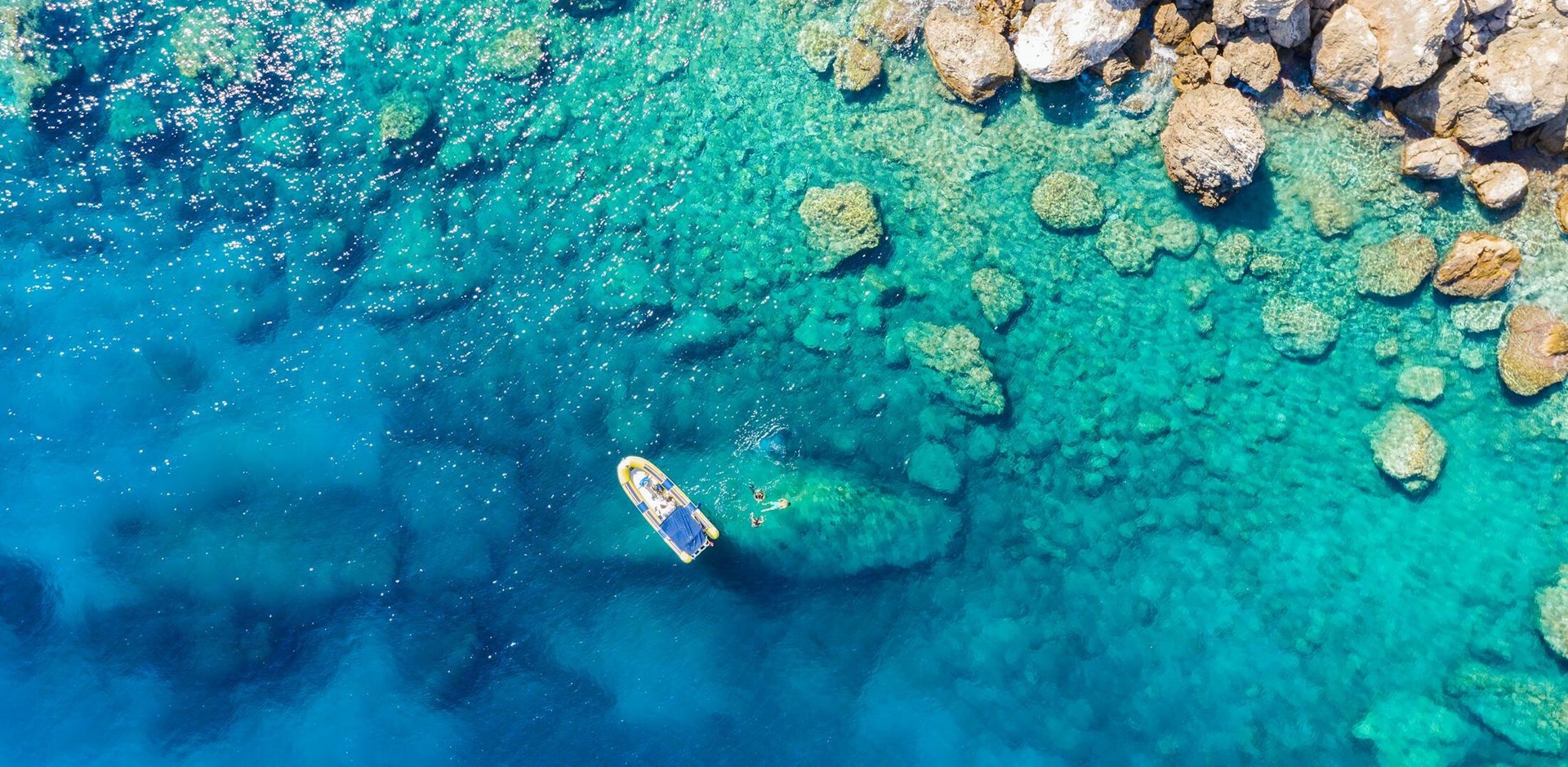 Aerial view of a rib boat with snorkelers and divers at the turquoise colored coast of the Aegean Sea in Greece