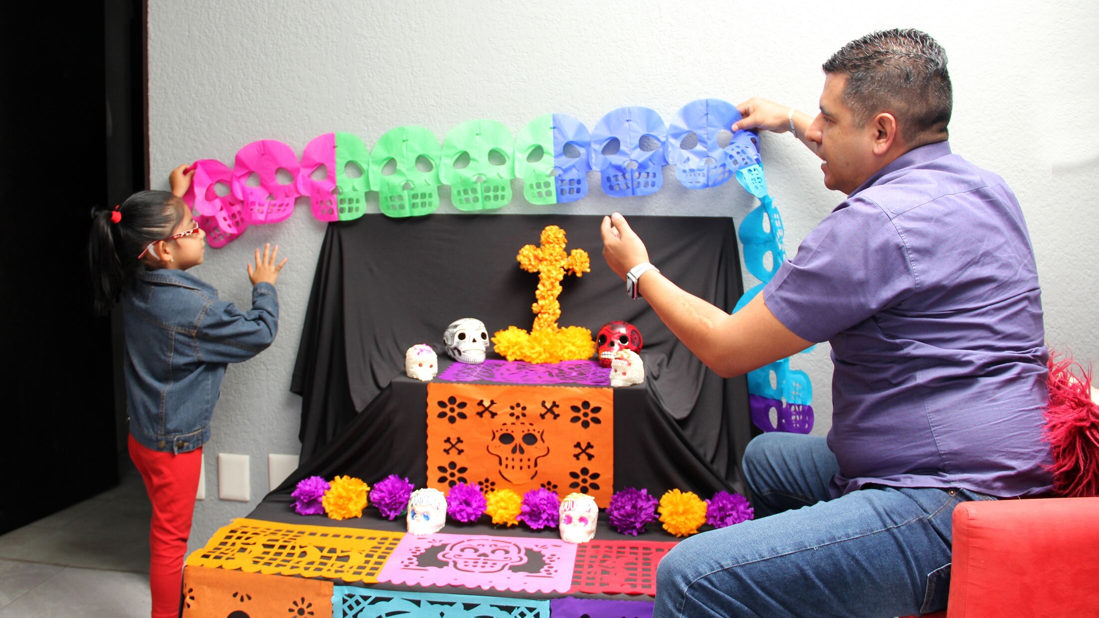 Mexican dad and daughter put the altar and offering of the Day of the Dead in their house for their deceased relatives part of the tradition and culture of Mexico