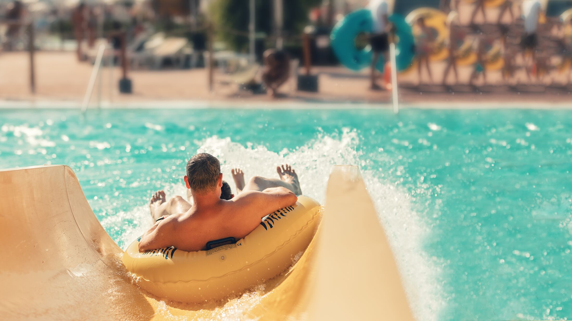 Cool people having fun on the water slide with friends and familiy in the aqua fun park glides playing happy and water splashes are all over. Blue sky background looks amazing sunlight