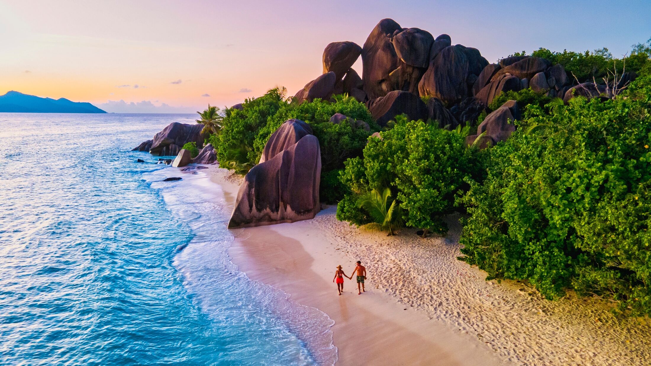 Anse Source d'Argent beach, La Digue Island, Seyshelles, Drone aerial view of La Digue Seychelles bird eye view.of tropical Island, couple men and woman walking at the beach during sunset at a luxury